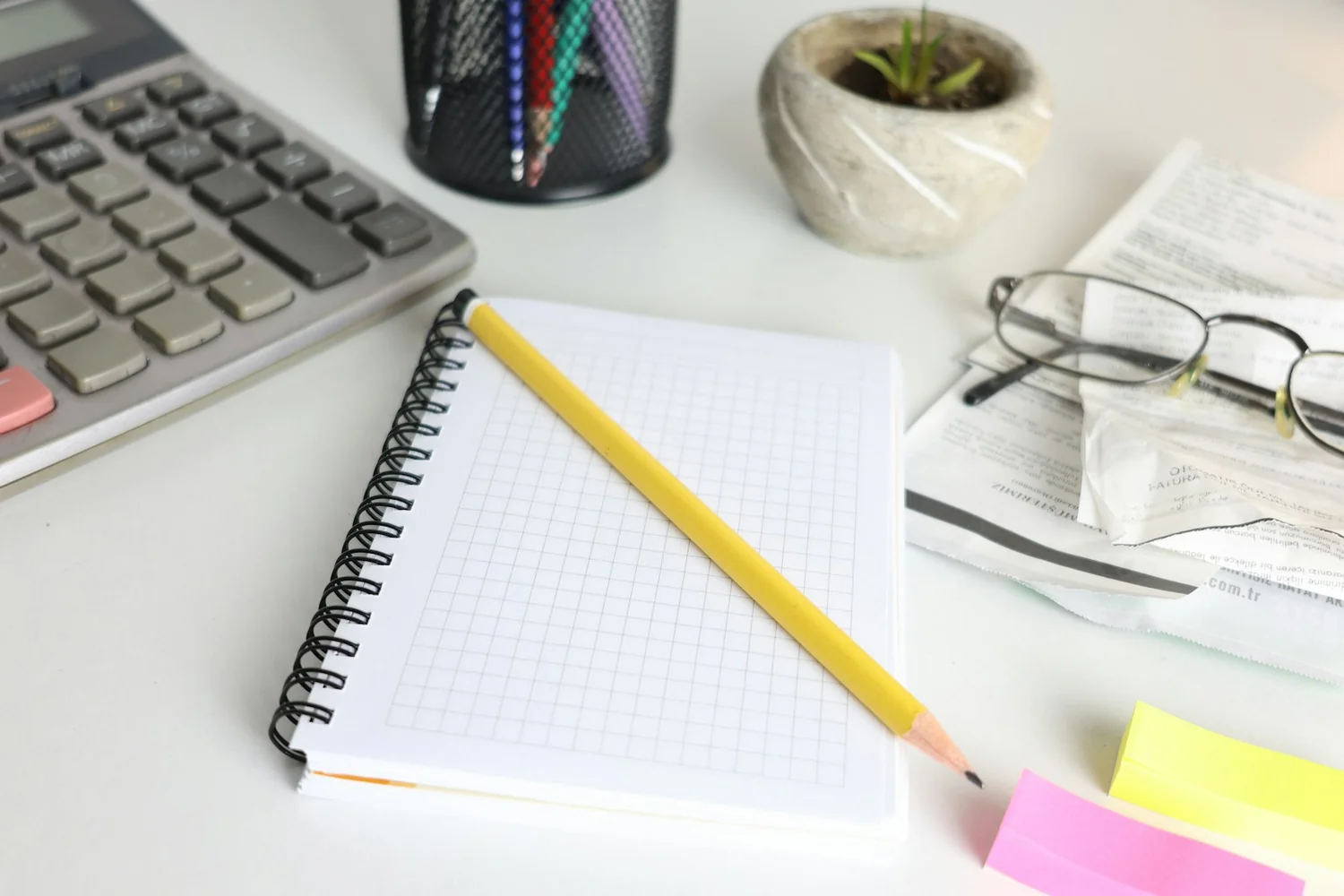 Calculatrice, carnet à spirale et lunettes posés sur un bureau clair