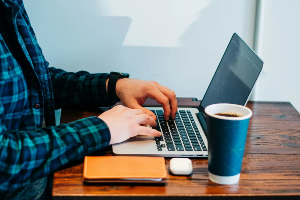 Personne en chemise à carreaux bleus et verts, assise devant un ordinateur portable, les mains posées sur le clavier